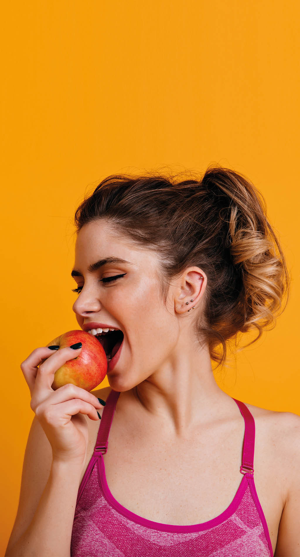 Indoor photo of blissful woman eating apple  Brunette fitness girl enjoying fruits 