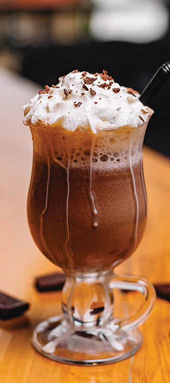 side view of chocolate milkshake with whipped cream in a glass on a wooden table