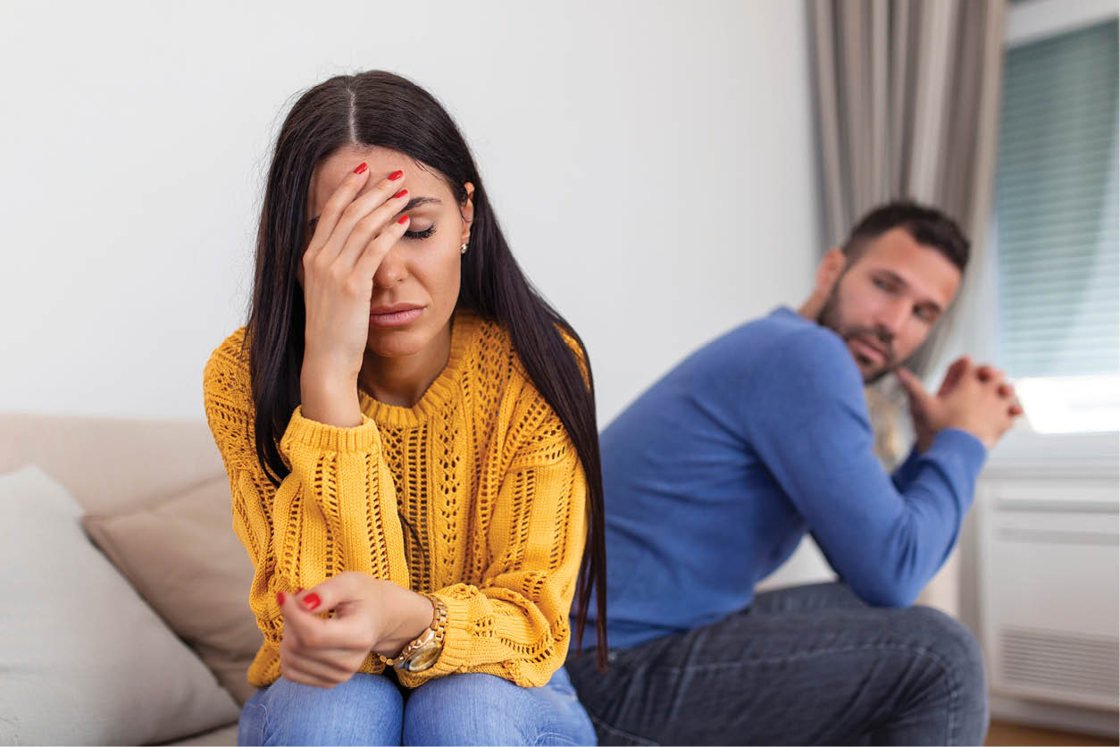 Sad pensive young girl thinking of relationships problems sitting on sofa with offended boyfriend, conflicts in marriage