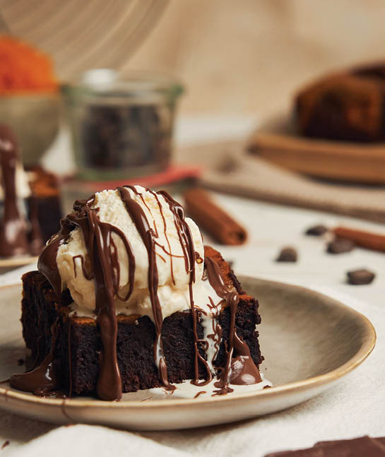 A closeup of a freshly baked delicious pumpkin chocolate brownie with ice cream on a plate