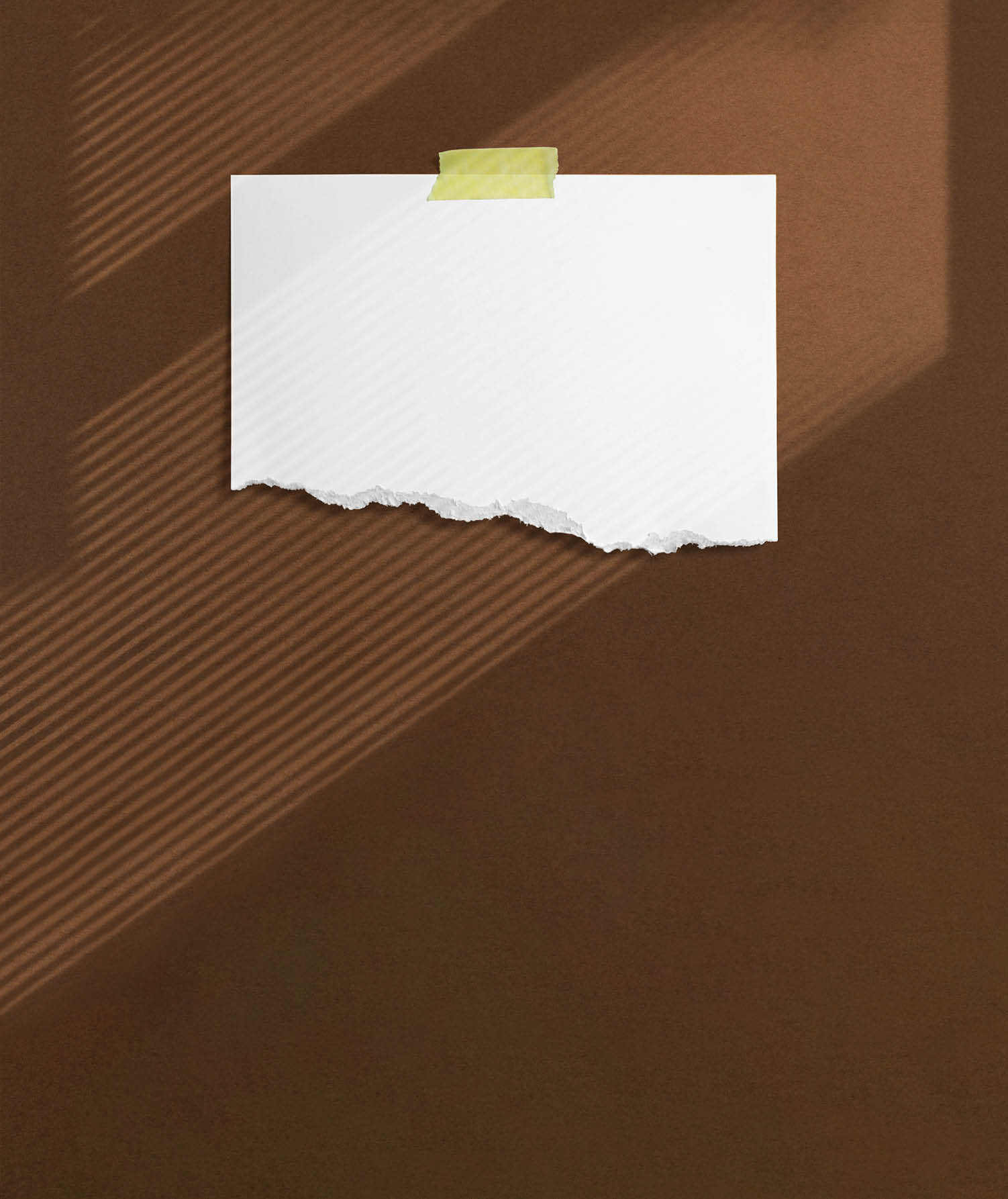 Blank torn paper frame glued with adhesive tape to brown textured wall with soft window shadows adobe as template for graphic designers presentations, portfolios etc.