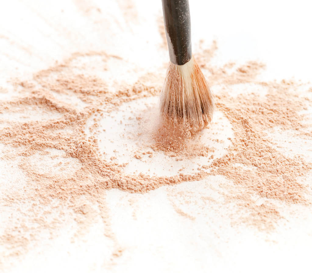 Close-up of crushed mineral shimmer powder golden color with makeup brush on white background