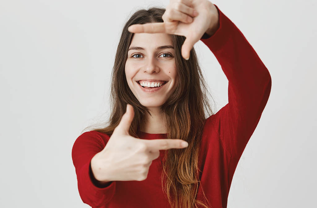 Happy enthusiastic young european girl with broad smile, making frame gesture in front of camera, isolated over white background  Student dreams to become well-known executive producer 