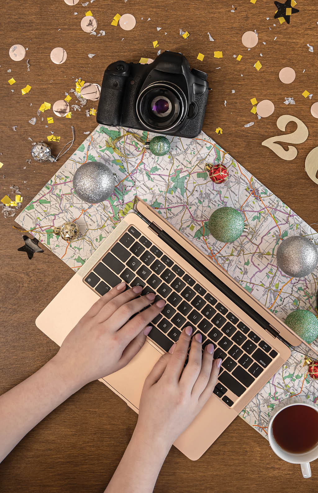 Christmas festive travel flat lay with numbers 2022, map, camera and laptop on wooden background 