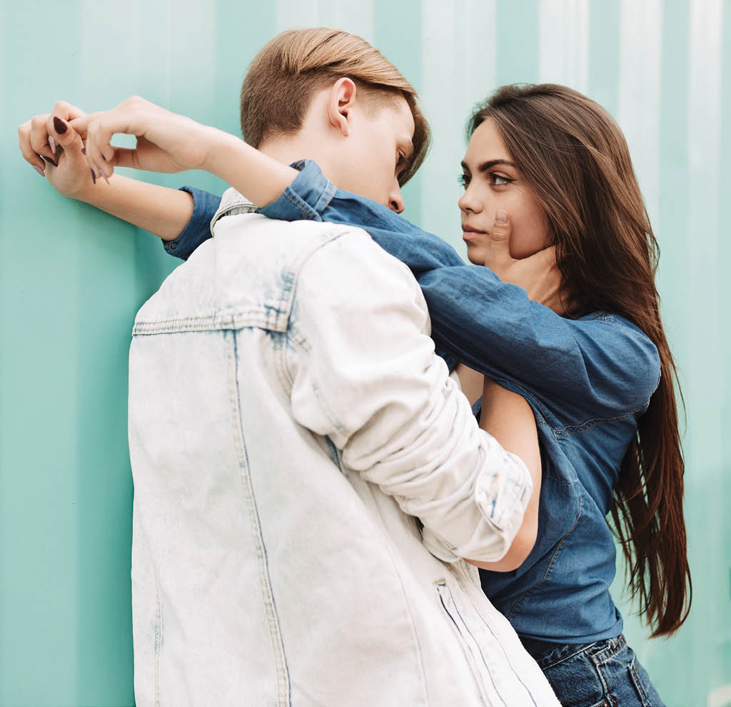 Portrait of young beautiful couple embracing each other while standing on over blue background  Pretty lady dreamily looking on her boyfriend