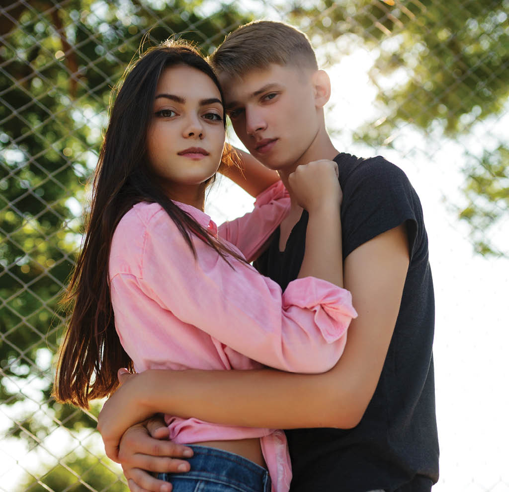 Portrait of beautiful couple standing and embracing one another while dreamily looking in camera in park