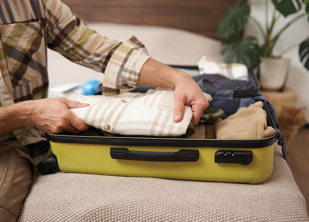 Cropped shot of hands packing clothes in luggage, going on vacation and prepared his suitcase, organises his items inside bag, packs for holiday 