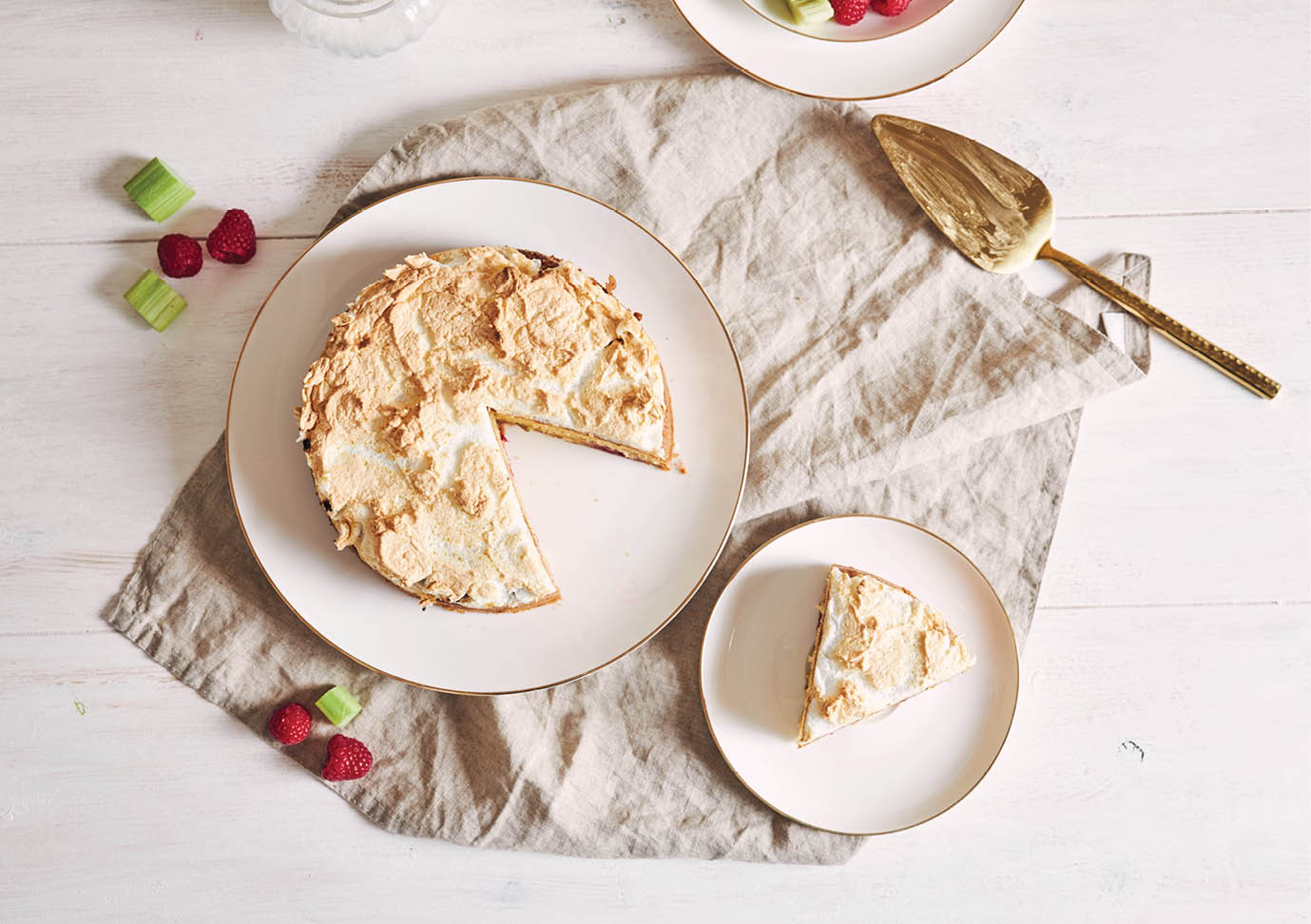 An overhead shot of a beautiful and delicious raspberry and rhubarb cake with ingredients on a table