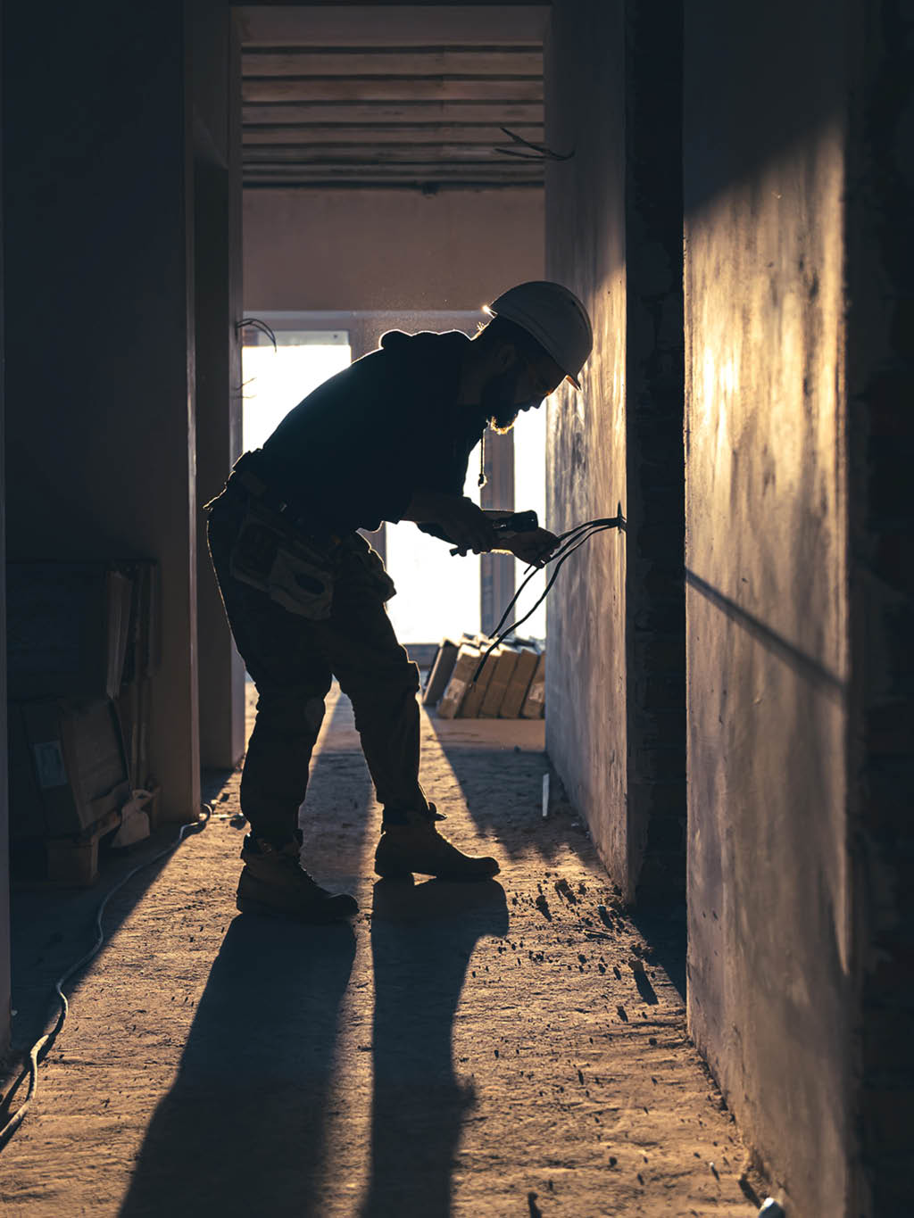 A construction electrician cuts a voltage cable during a repair, silhouette in the light of the setting sun 