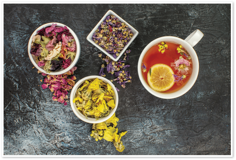 close up photo of herbal tea near bowls of dry flowers on grey background