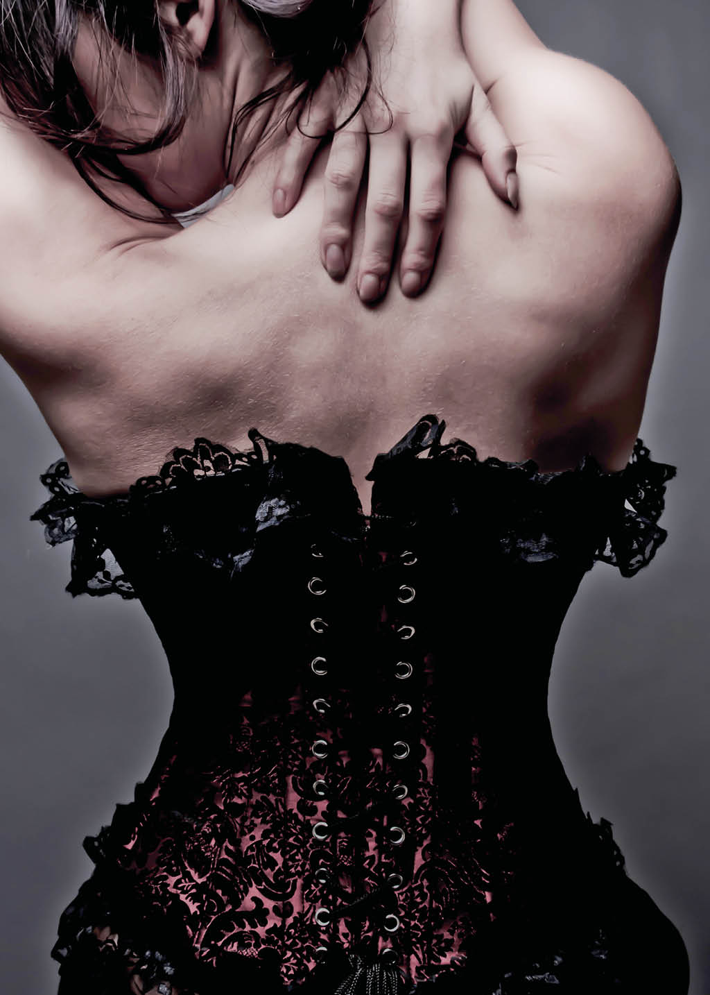 A woman wearing a black corset, with her hands on her back.