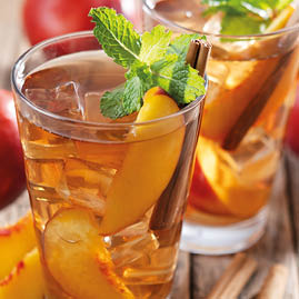 Refreshing peach iced tea in glass with ice cubes and cinnamon on wooden table
