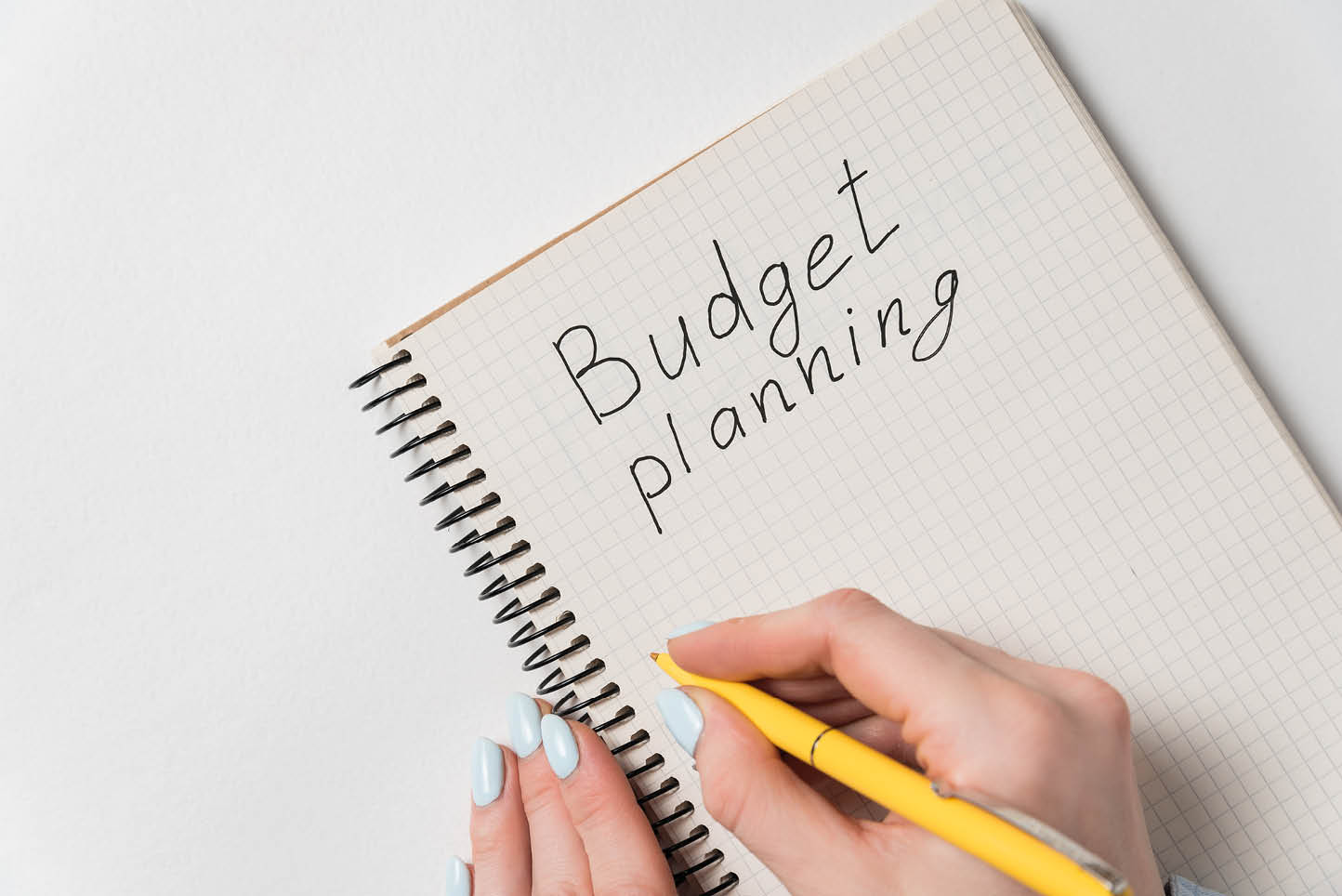 Budget planning concept. Female hand holding pen and writing in notebook. White background.