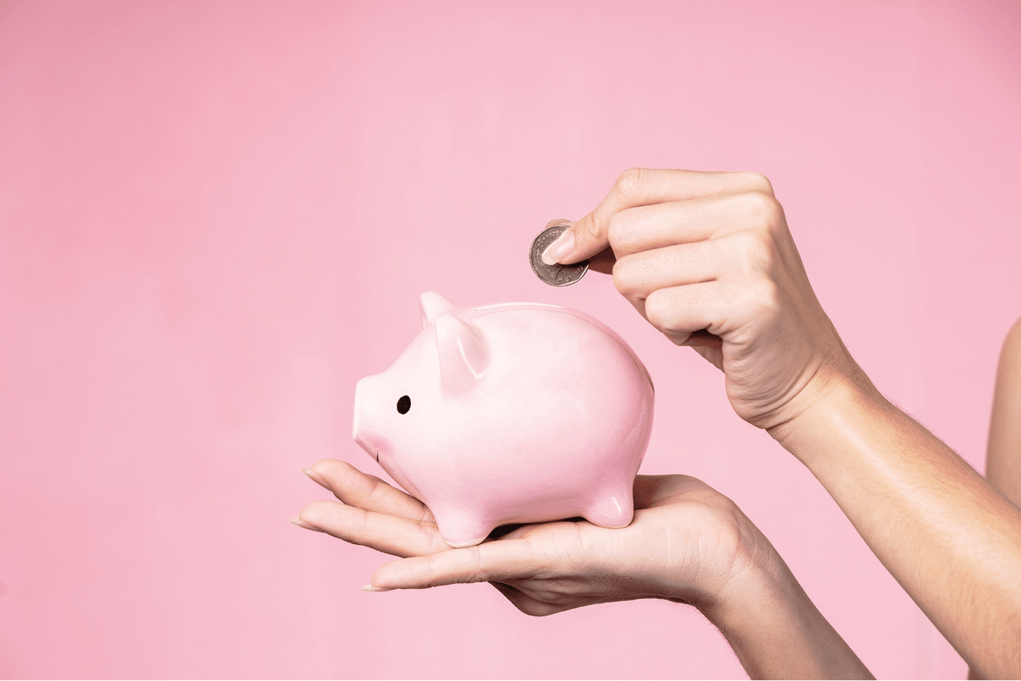 Closeup of hands putting coin into a piggy bank. Saving concept.