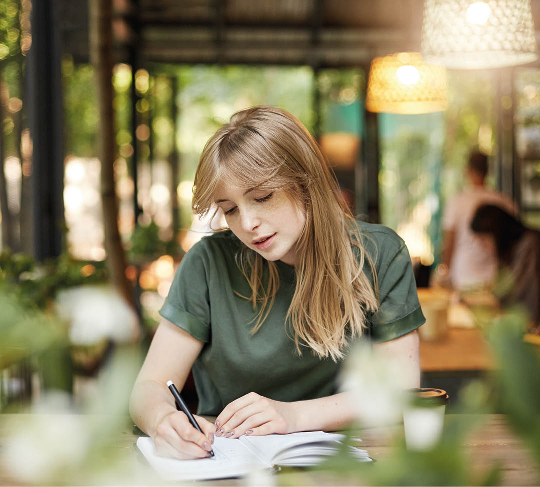 Portrait of a young blonde student girl reading her notes drinking coffee in a cafe outdoors waiting for her classes smiling. Copy space.