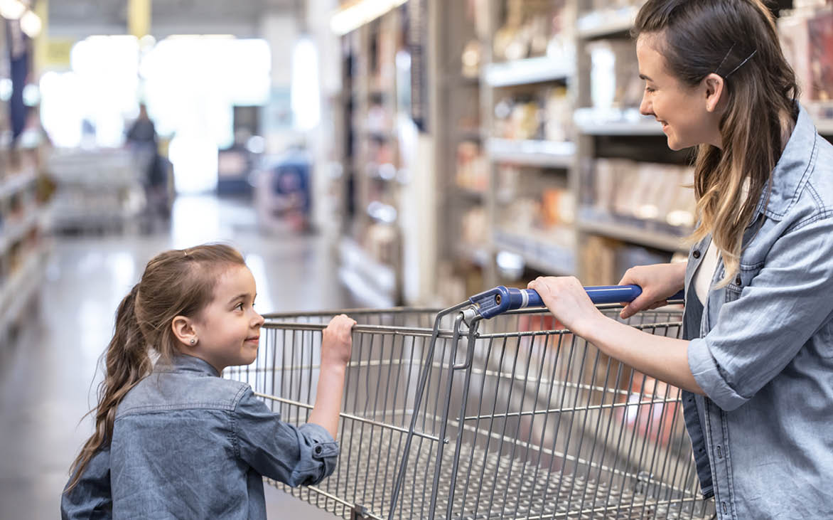 Mother and daughter in blue shirts shopping in supermarket using cart
