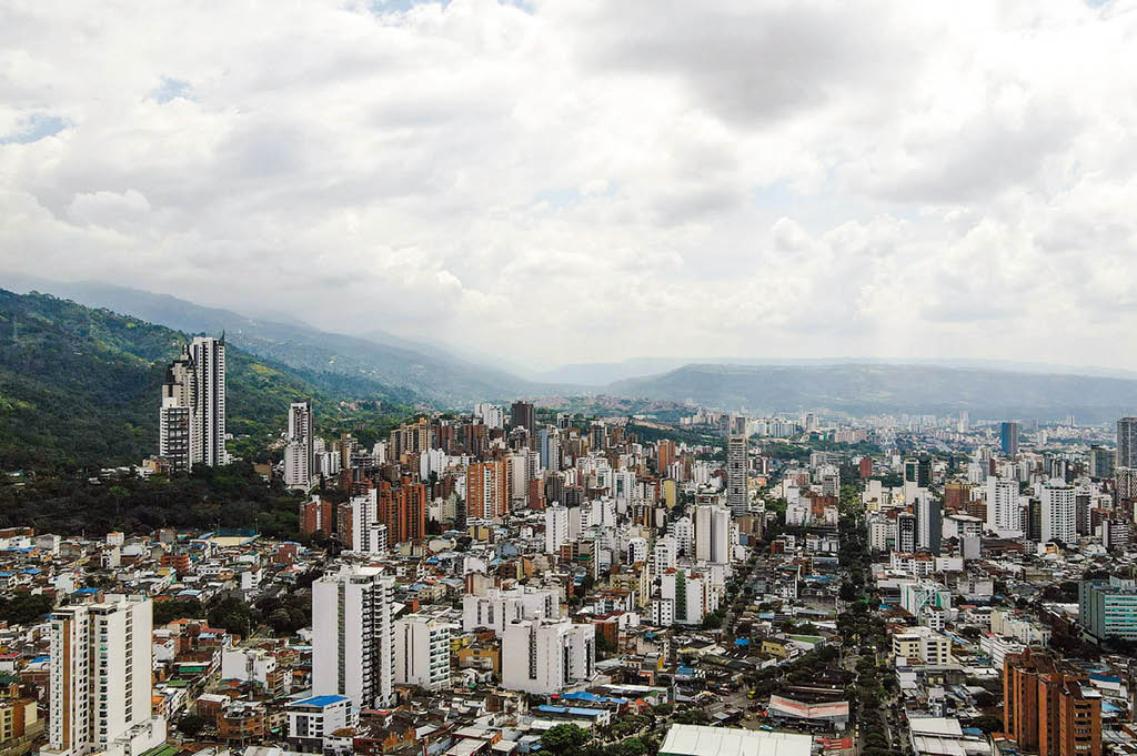 Ciudad con numerosos edificios altos y monta as verdes al fondo bajo un cielo nublado. Descripci n generada con IA