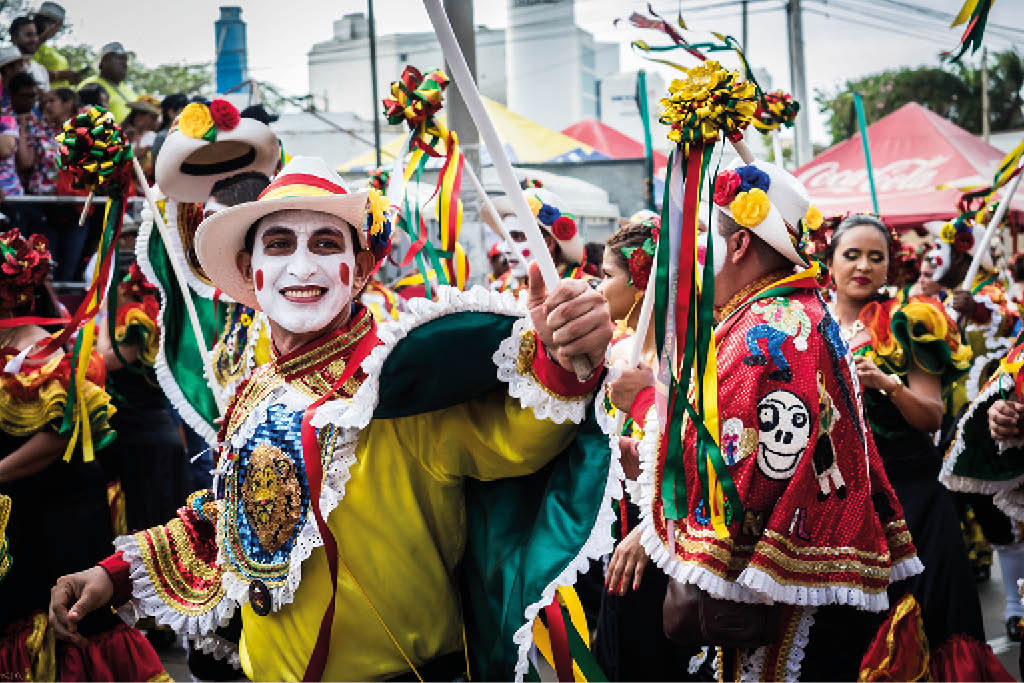 Personas vestidas con trajes coloridos y adornados con cintas y flores participan en una celebraci n tradicional al aire libre. Descripci n generada con IA