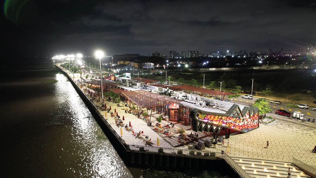 Un muelle iluminado de noche con una estructura moderna decorada con luces y personas caminando alrededor junto a un cuerpo de agua. Descripci n generada con IA