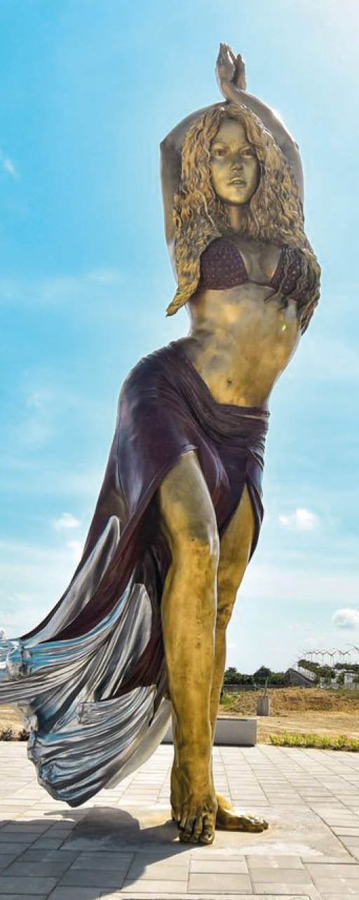 Escultura dorada de una persona con vestido largo y brazos levantados en un espacio abierto con cielo azul y nubes. Descripci n generada con IA