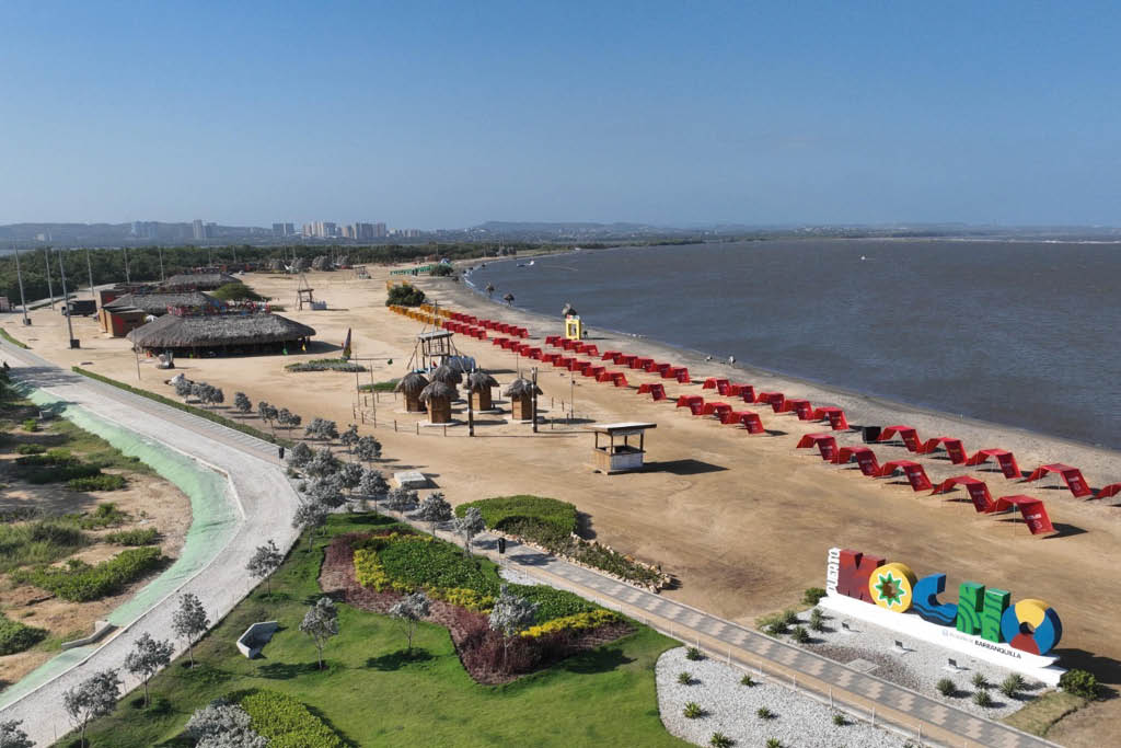 Playa con sombrillas rojas alineadas, estructuras de madera, reas verdes y un letrero colorido que dice “Cabo" junto al mar bajo un cielo despejado.  Descripci n generada con IA