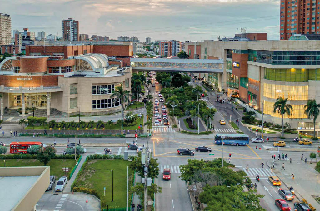 Vista a rea de una intersecci n urbana con edificios modernos, veh culos en movimiento y personas cruzando las calles al atardecer. Descripci n generada con IA