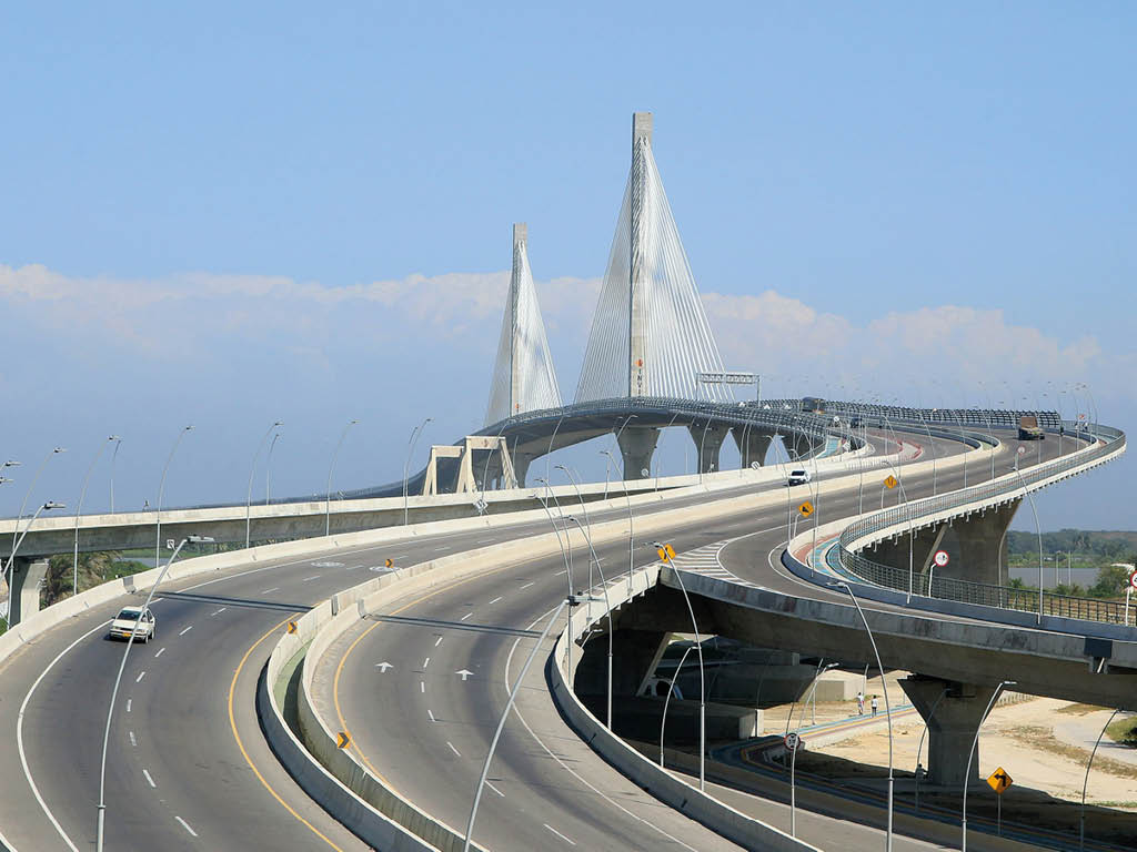 Un puente moderno con estructura de cables y varios carriles de tr fico se extiende sobre un paisaje despejado bajo un cielo azul. Descripci n generada con IA