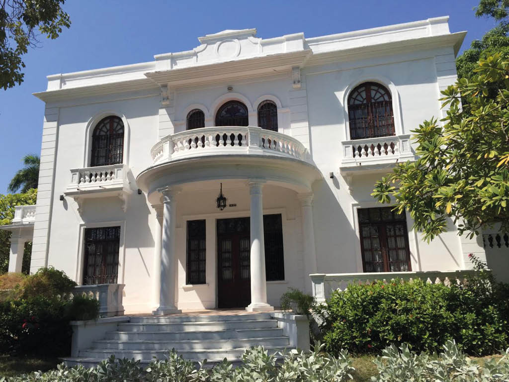 Edificio blanco de estilo cl sico con columnas y balcones en un d a soleado. Descripci n generada con IA