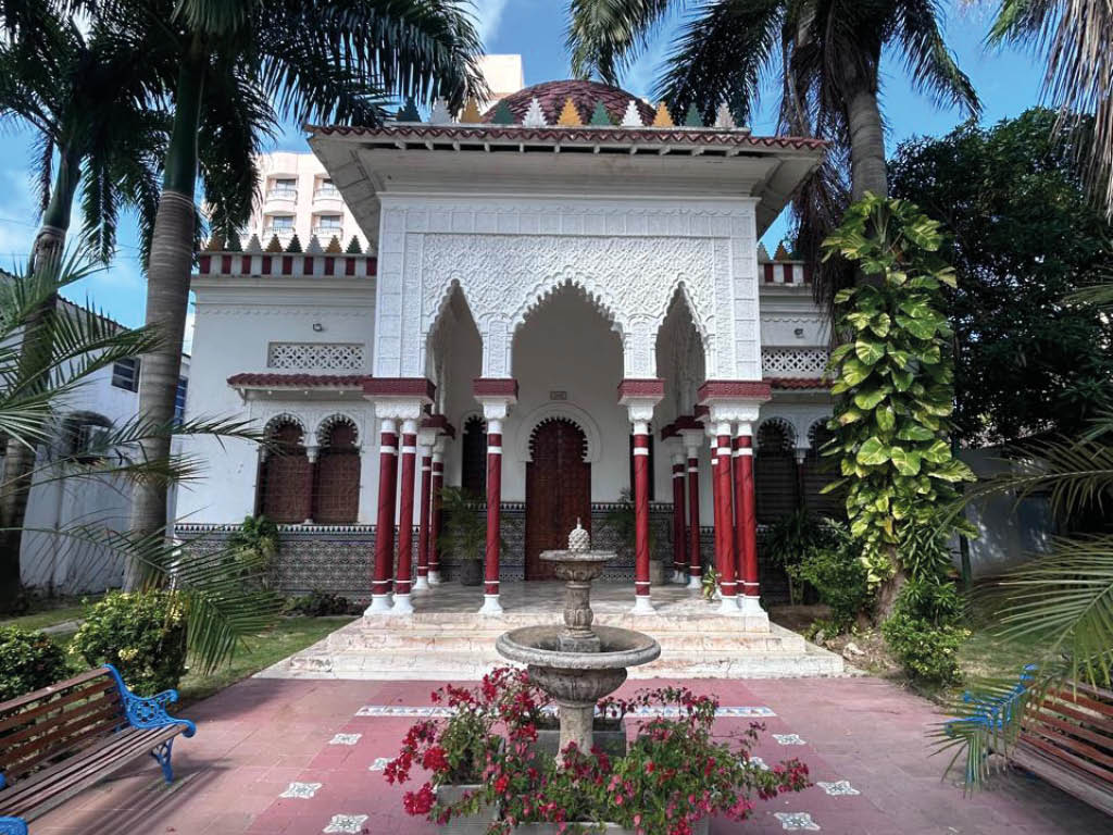 Edificio con arquitectura de estilo isl mico rodeado de palmeras bajo un cielo azul despejado. Descripci n generada con IA