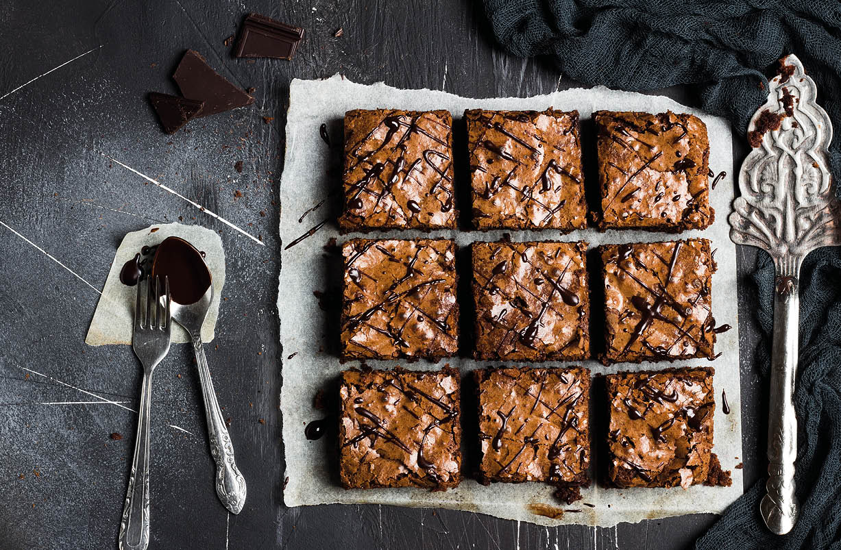 Chocolate brownie cake piece pie homemade pastries sweet cooking with spoon of melted chocolate on dark background top view flat lay