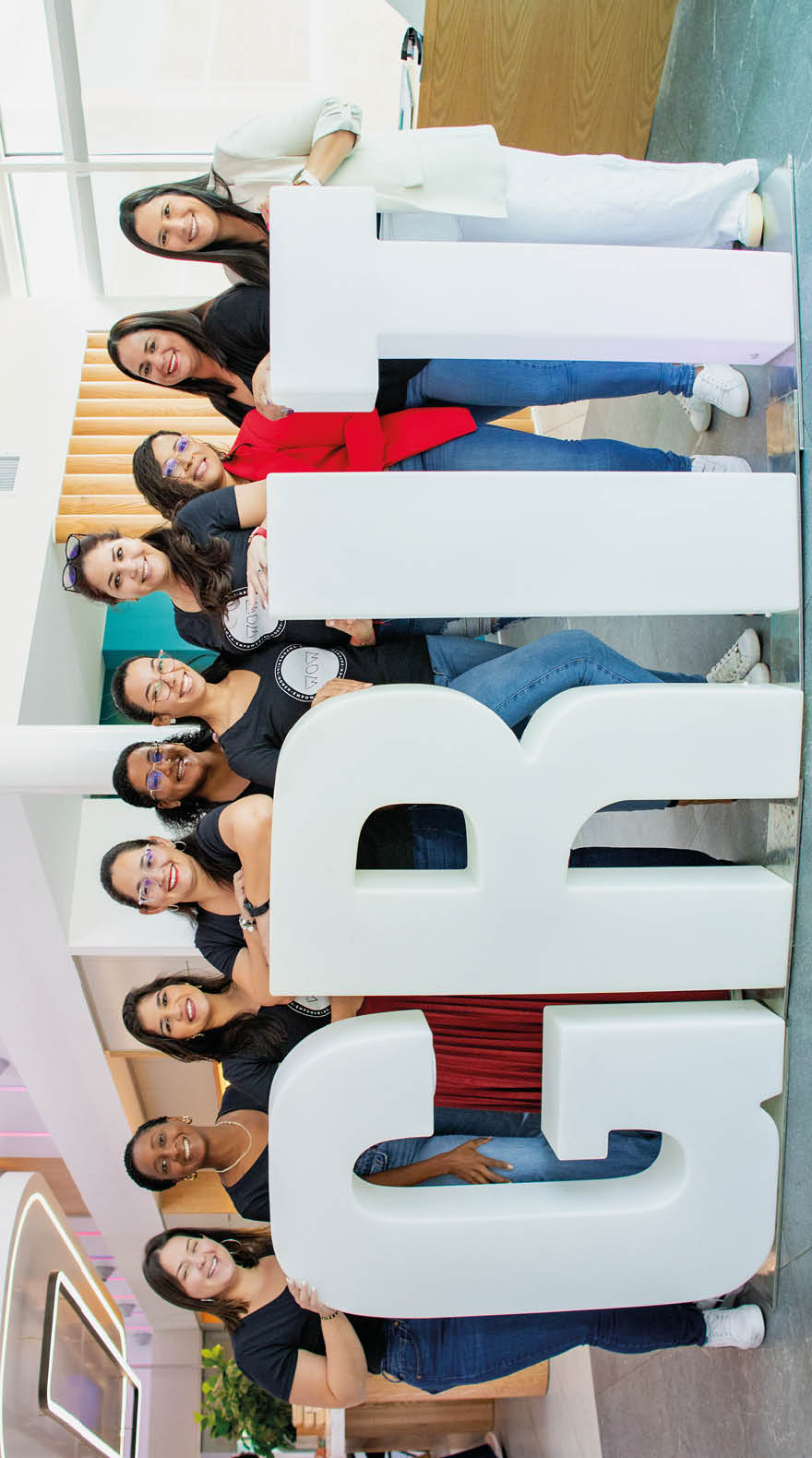 Ocho personas sonrientes posan juntas detr s de grandes letras blancas en un espacio interior bien iluminado. Descripci n generada con IA