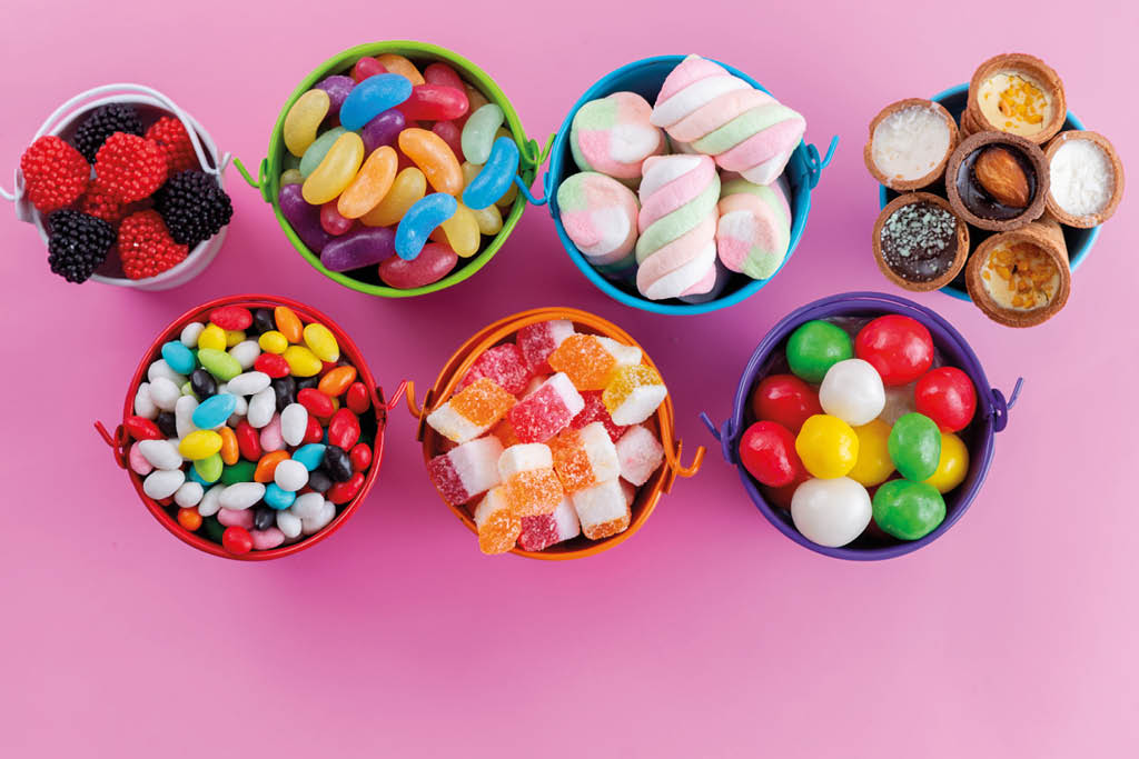 Siete peque os baldes de colores contienen diferentes tipos de dulces variados sobre un fondo rosa. Descripci n generada con IA