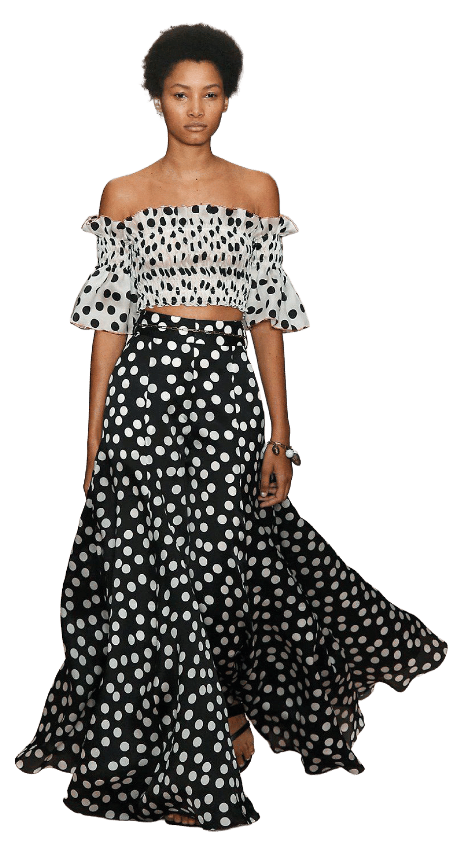 Persona con cabello corto y rizado lleva un conjunto de dos piezas con blusa corta de hombros descubiertos y falda larga negra con estampado de lunares blancos. Descripci n generada con IA