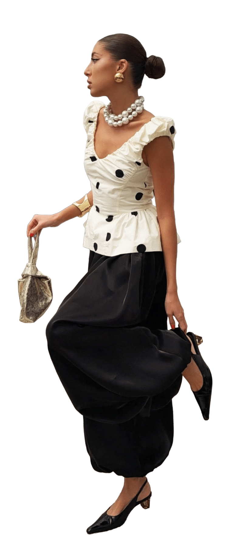 Persona con peinado recogido lleva blusa blanca con lunares negros y volantes, falda o pantal n negro amplio, zapatos de tac n bajo, collar de perlas grandes, aretes dorados y sostiene un bolso peque o. Descripci n generada con IA