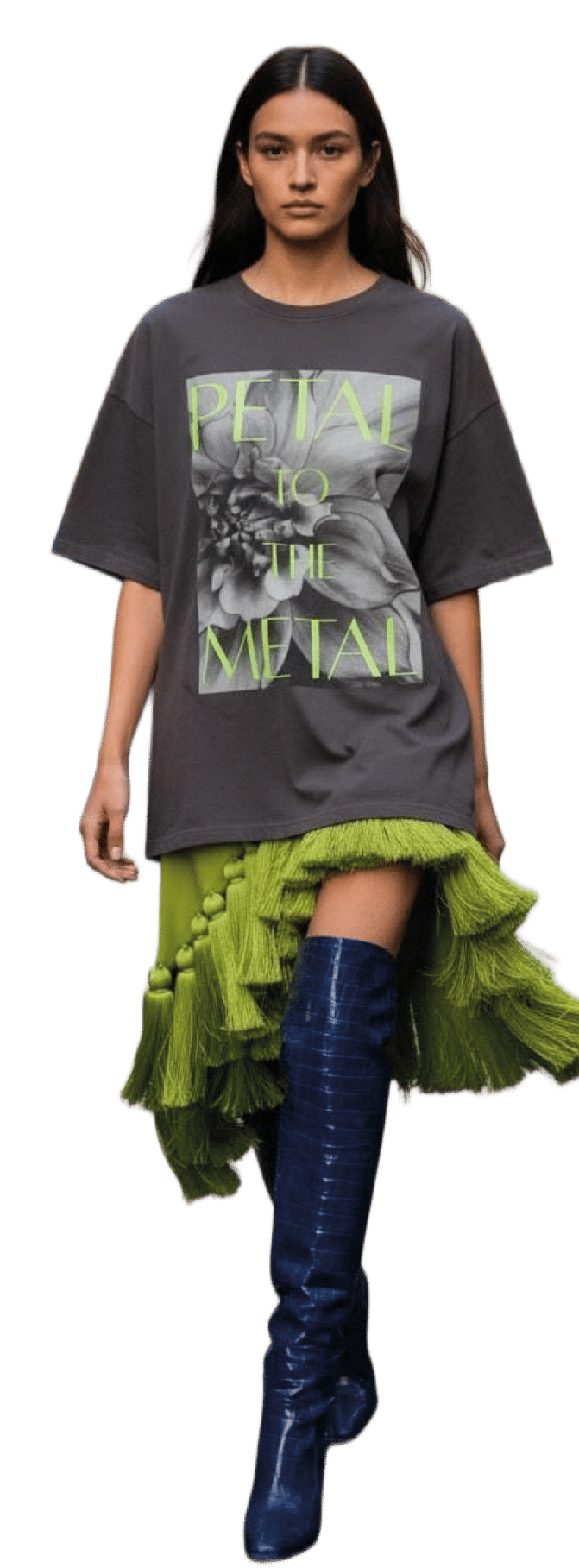 Persona con cabello largo y lacio que lleva una camiseta gris oversize con texto y una falda verde con volantes asim trica combinada con botas altas azul oscuro. Descripci n generada con IA