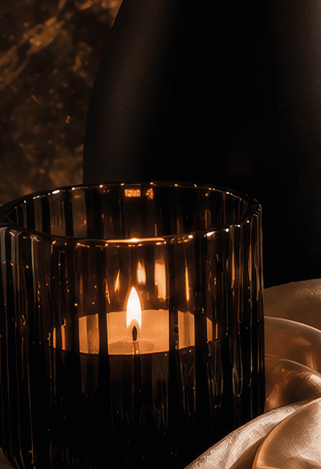 Un conjunto elegante de objetos decorativos y de moda sobre una superficie satinada que incluye un ramo de flores secas, velas encendidas, un perfume, joyas, un bol grafo y un cuaderno con un coraz n dibujado, junto a un zapato de tac n alto negro. Descripci n generada con IA
