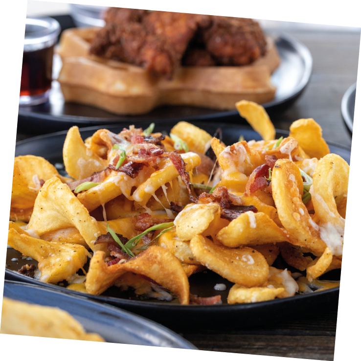 A selective focus shot of French fries with melted cheese and sliced sausage on a wooden table