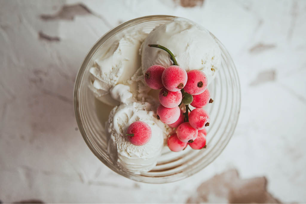 Cranberries and ice cream in a glass cup top view on a white textured background 