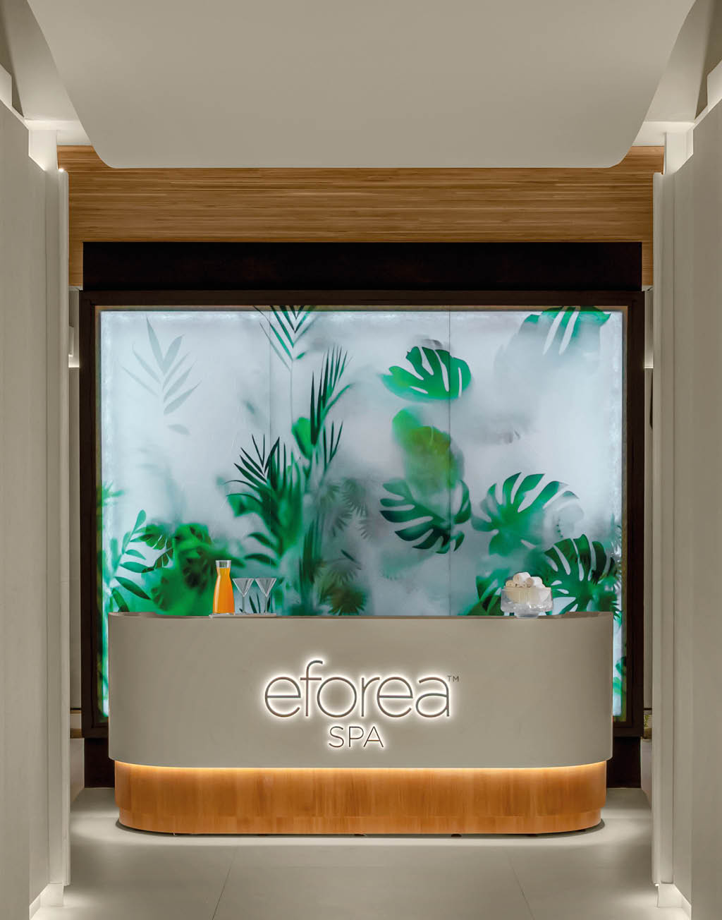 Pasillo iluminado con paredes decoradas con plantas verdes y un mostrador con el logo de eforea spa al fondo. Descripci n generada con IA