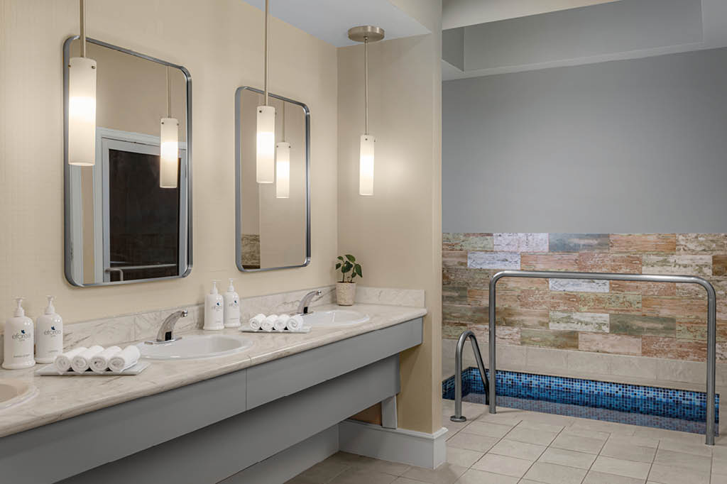 Ba o moderno con dos lavabos, espejos rectangulares, luces colgantes y una peque a piscina interior con azulejos decorativos. Descripci n generada con IA