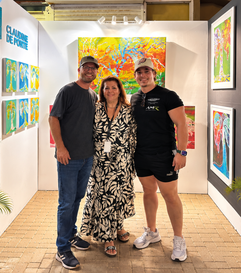 Tres personas sonrientes posan juntas en un espacio de exhibici n de arte con pinturas coloridas en las paredes y plantas decorativas a los lados. Descripci n generada con IA