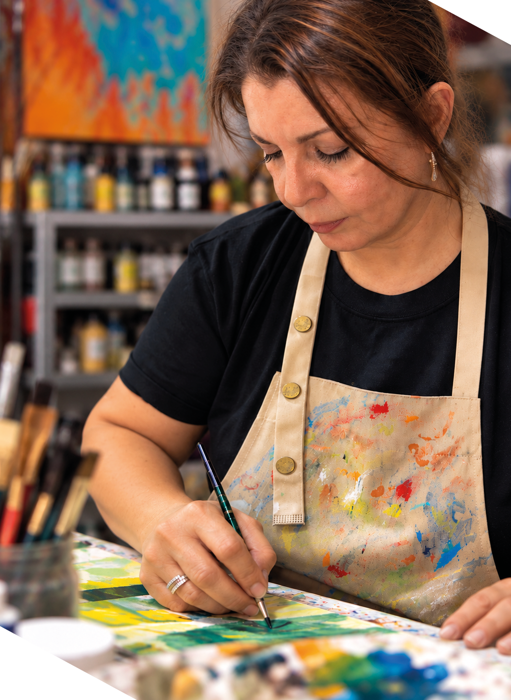 Una persona con delantal manchado de pintura est concentrada pintando sobre una superficie con un pincel en un taller de arte.  Descripci n generada con IA