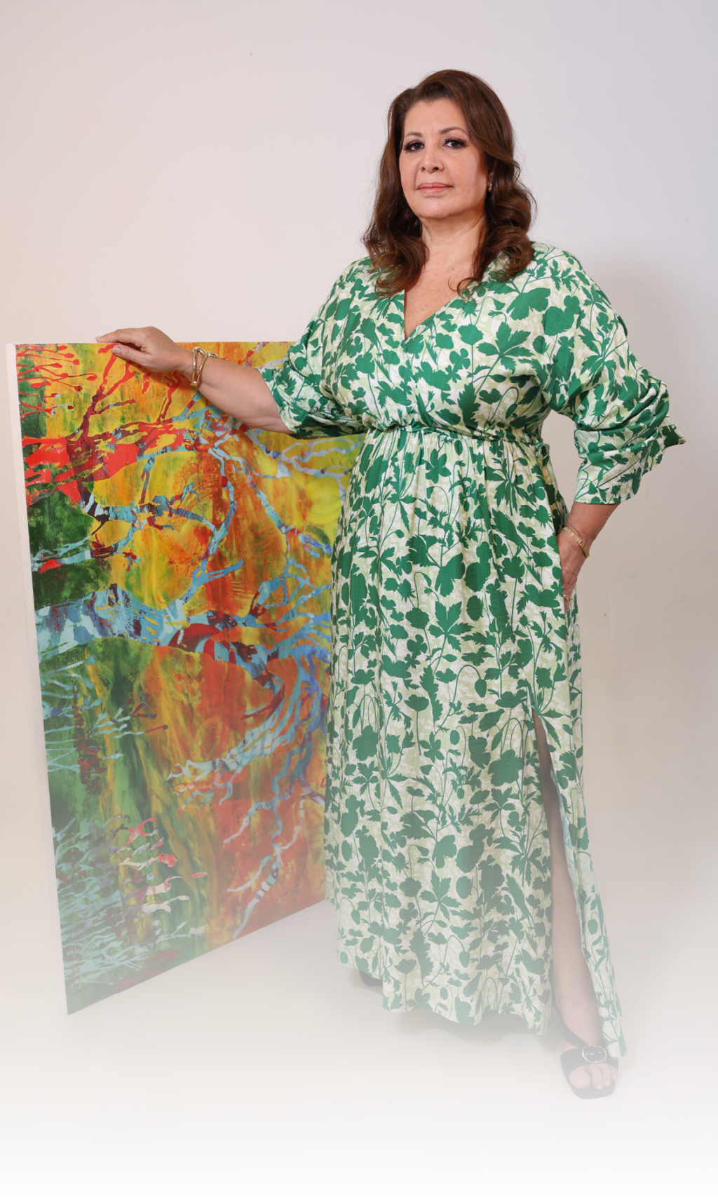Persona con cabello ondulado y vestido largo blanco con estampado verde que sostiene un cuadro colorido con motivos abstractos. Descripci n generada con IA