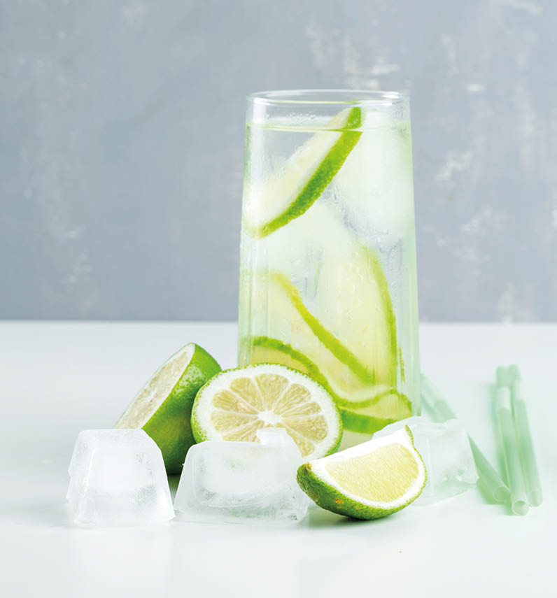 Lemonade in a glass with lemon, straws, ice cubes side view on white and plaster background 